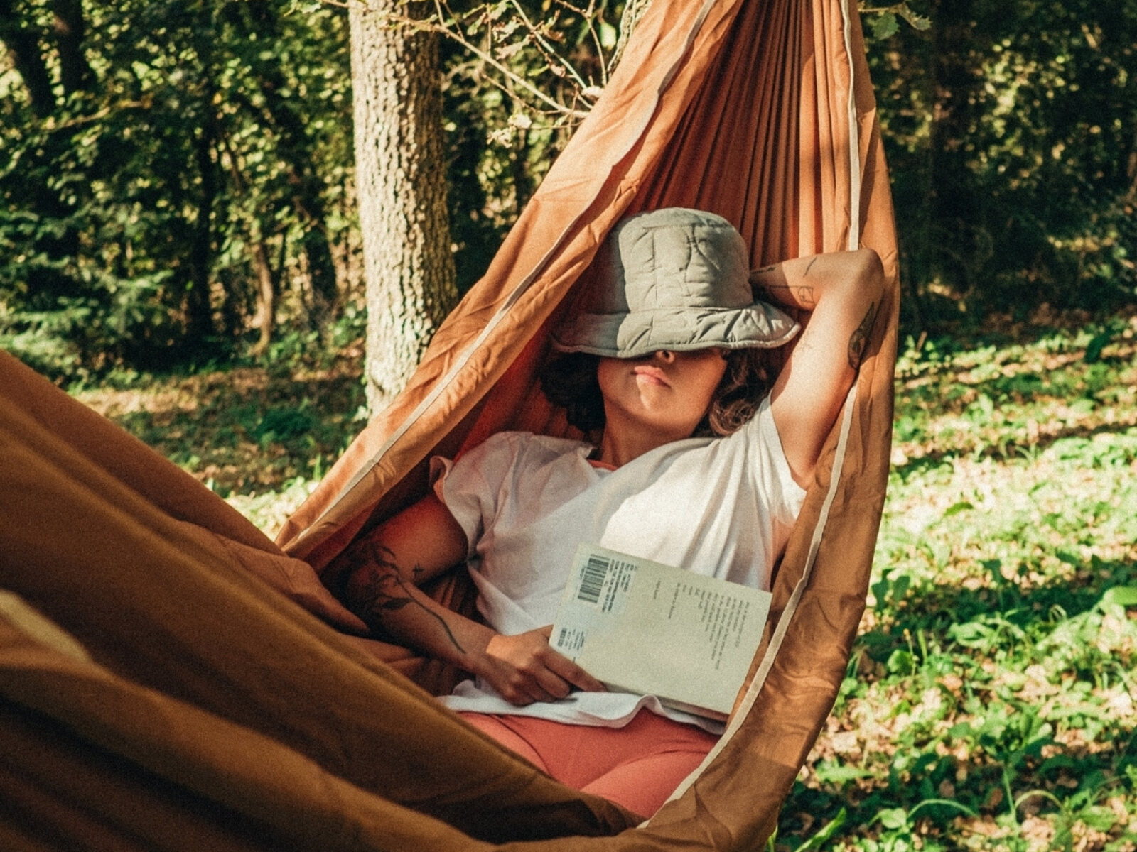 Resting in a hammock in dappled woodland light, a book set down